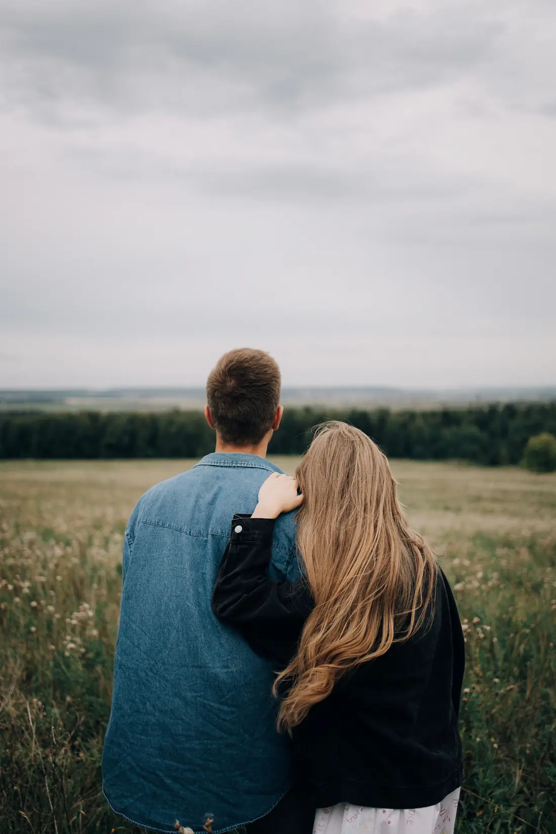A couple seen from behind, standing close together looking out over a field